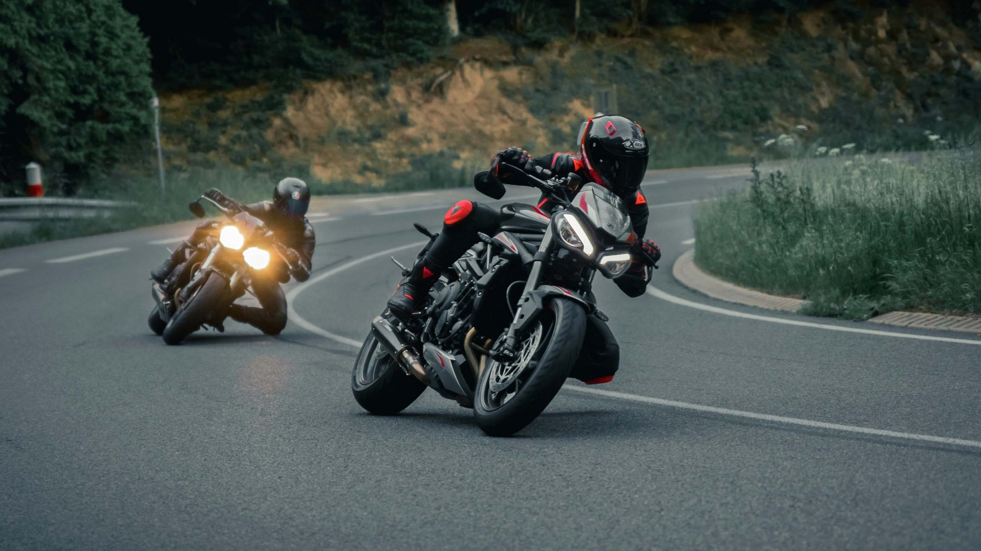 Ihr Motorradhotel im Bayerischen Wald Zwei Motorradfahrer in schwarzer Ausrüstung fahren auf kurviger Straße durch Wald