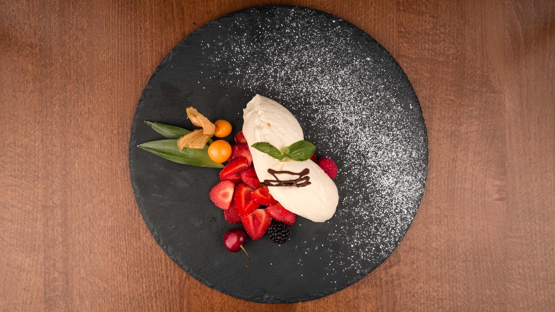 Genusspension: das Extra an Genuss Dessert mit Sahne, frischen Beeren und Puderzucker auf schwarzem Teller