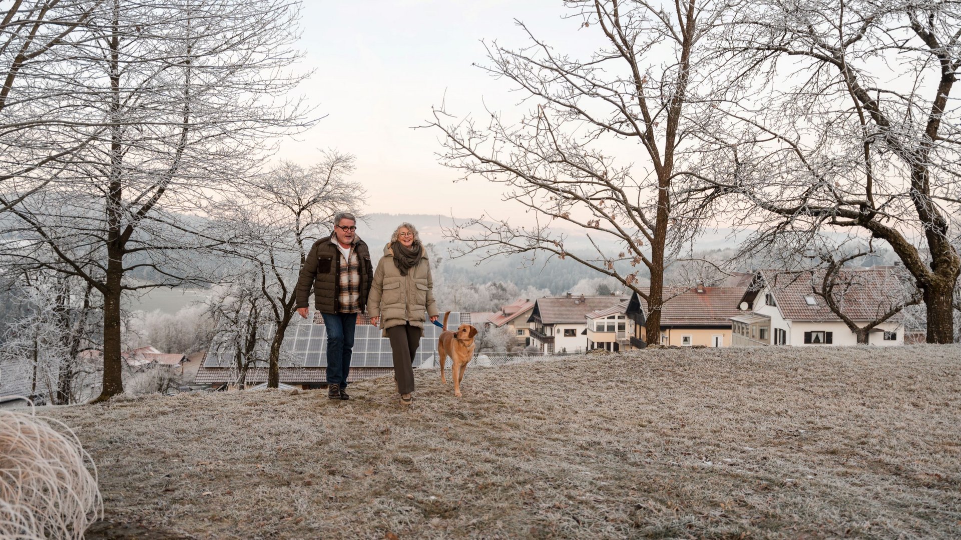 Den Bayerischen Wald spüren Älteres Paar geht mit Hund in winterlicher Landschaft spazieren