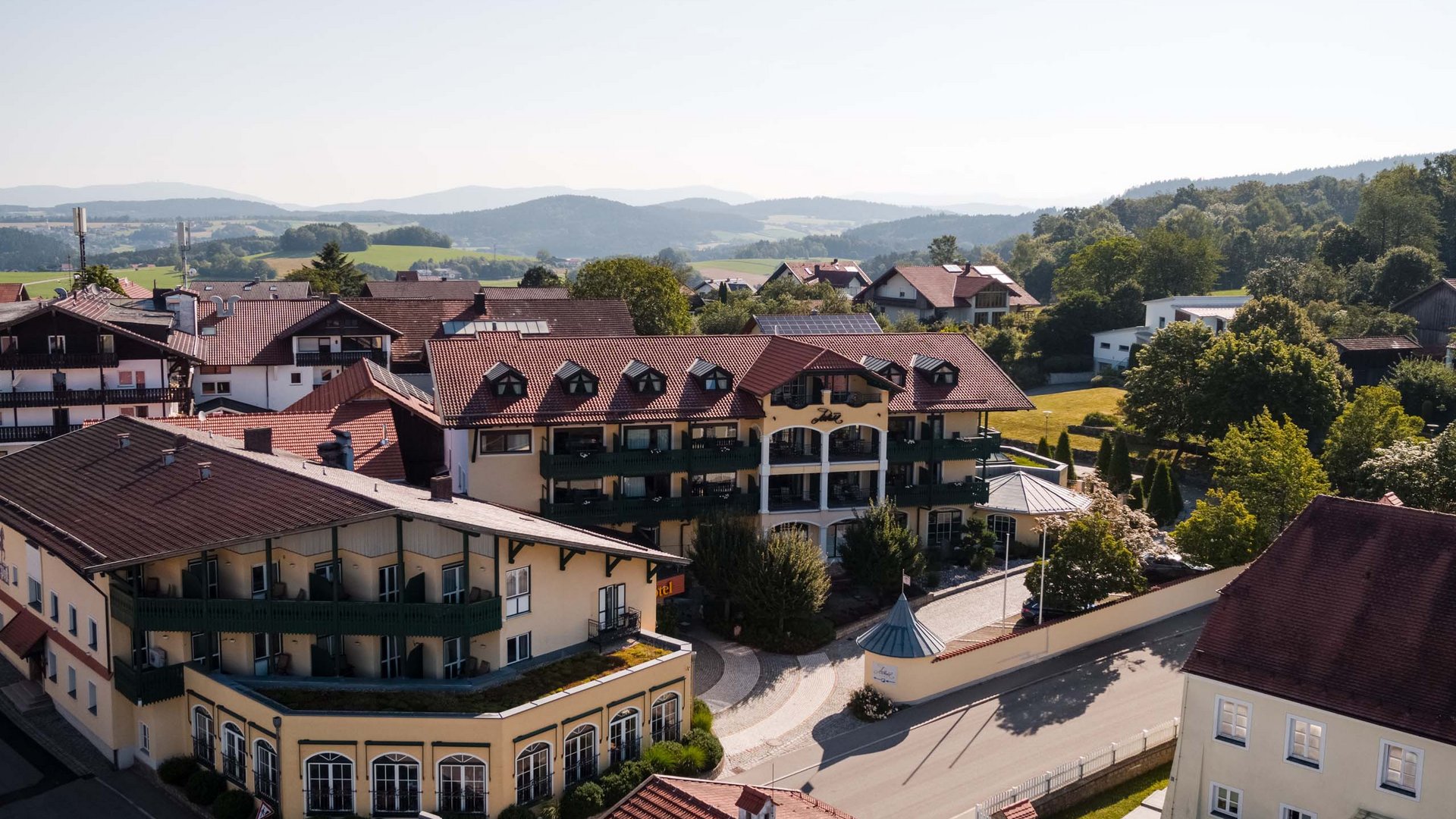 Luftaufnahme eines Dorfes mit traditionellen Gebäuden und grüner Landschaft im Hintergrund