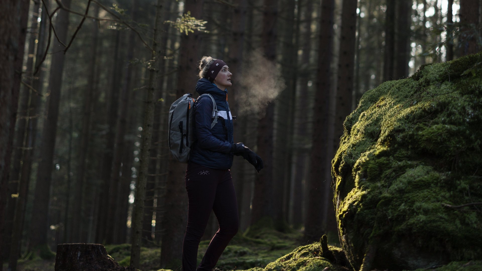 Frau steht im Wald und Sonne scheint auf das gruene Moos